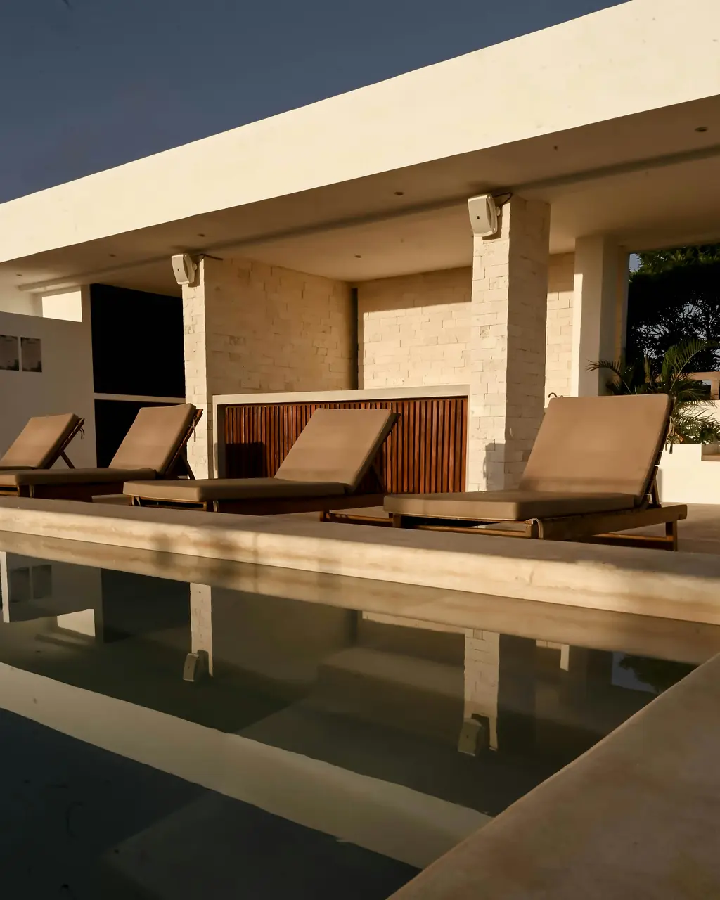 Loungers beside a long pool at sunset in Tulum